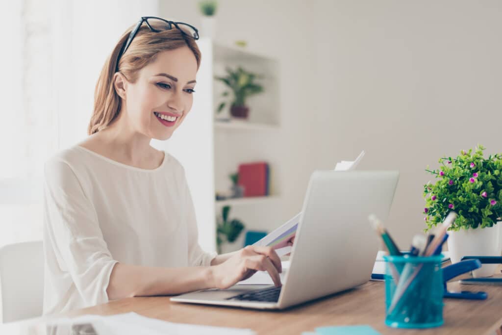 Woman smiling and typing on a laptop at home.