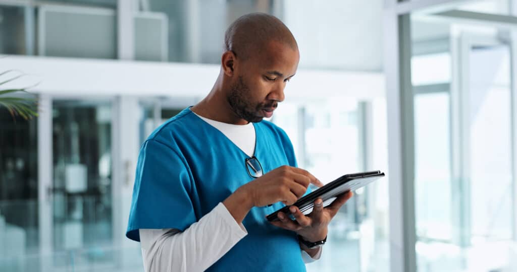 How Secure Patient Messaging Improves Care Coordination Black man, nurse and clinic with tablet on telehealth for patient appointment, consultation and information. Male person, employee and serious with browsing internet for healthcare, data and records.