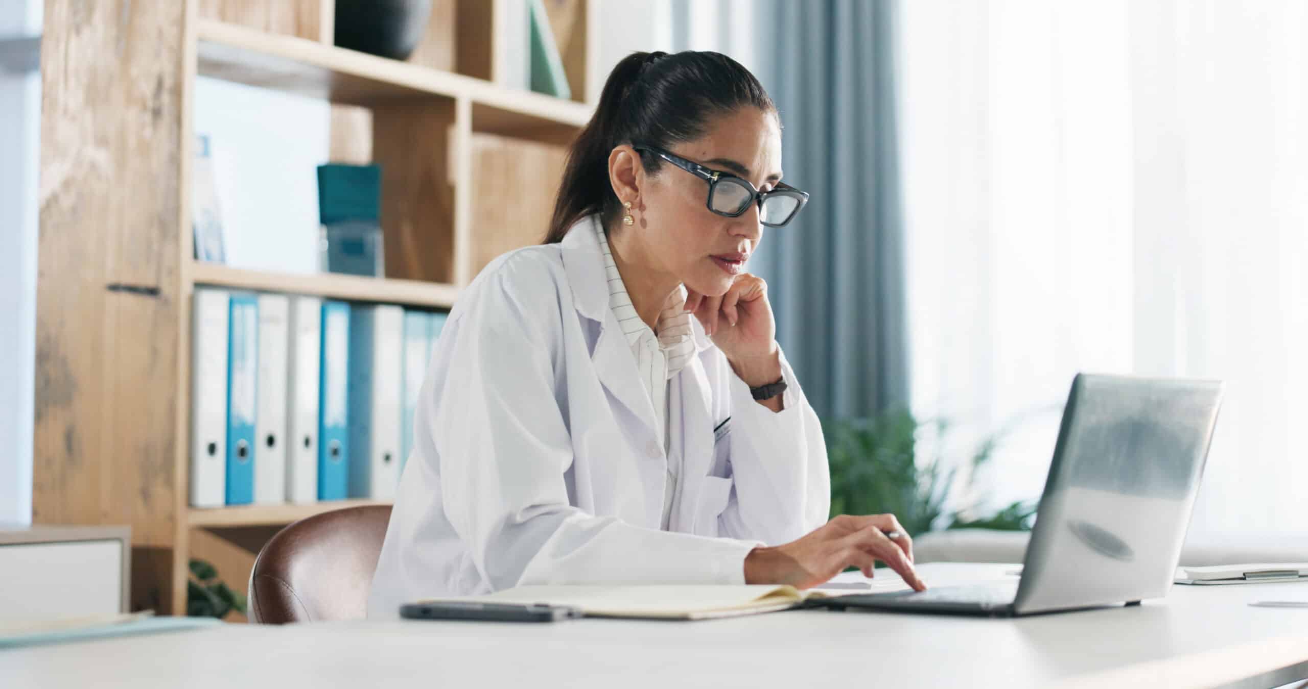 Research, woman and doctor with laptop in hospital for medical report or diagnostic information. Thinking, computer and female healthcare worker with brainstorming for treatment plan in clinic office.