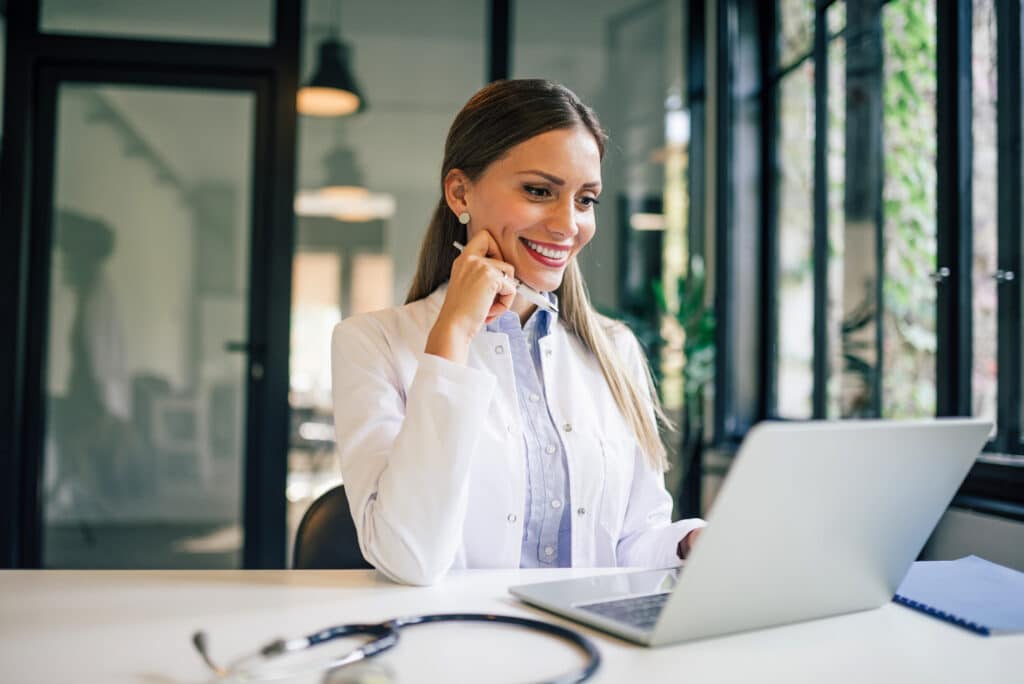 Portrait of a smiling female doctor looking at laptop in medical office.