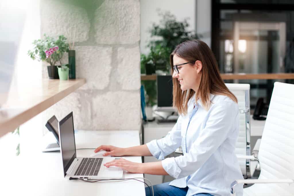 Young woman working at hotel reception. Employees workplace in modern office. Girl using laptop indoors. Social distancing for staff during quarantine.
