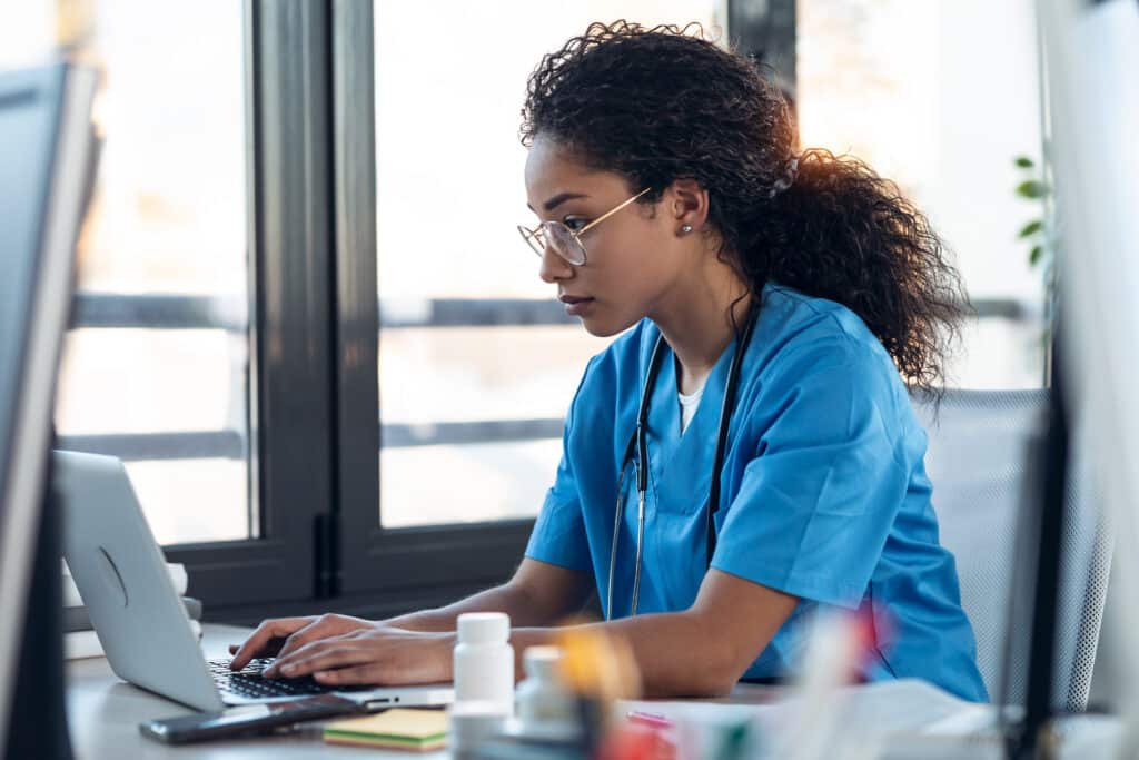 Shot of attractive young afro female doctor talking working with her computer in the consultation.
