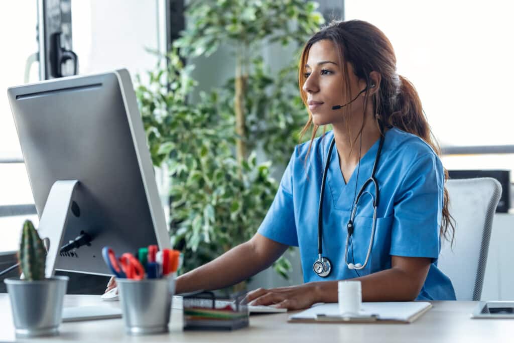Shot of female doctor talking with earphone while explaining medical treatment to patient through a video call with computer in the consultation.