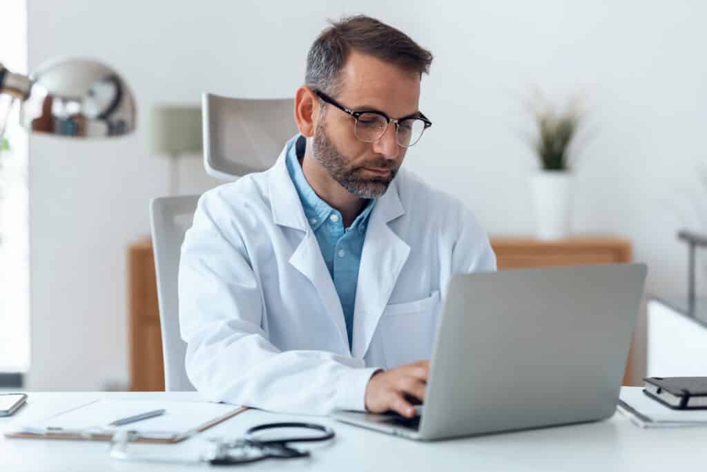 Shot of mature concentrated attractive male doctor working with her computer in medical consultation.