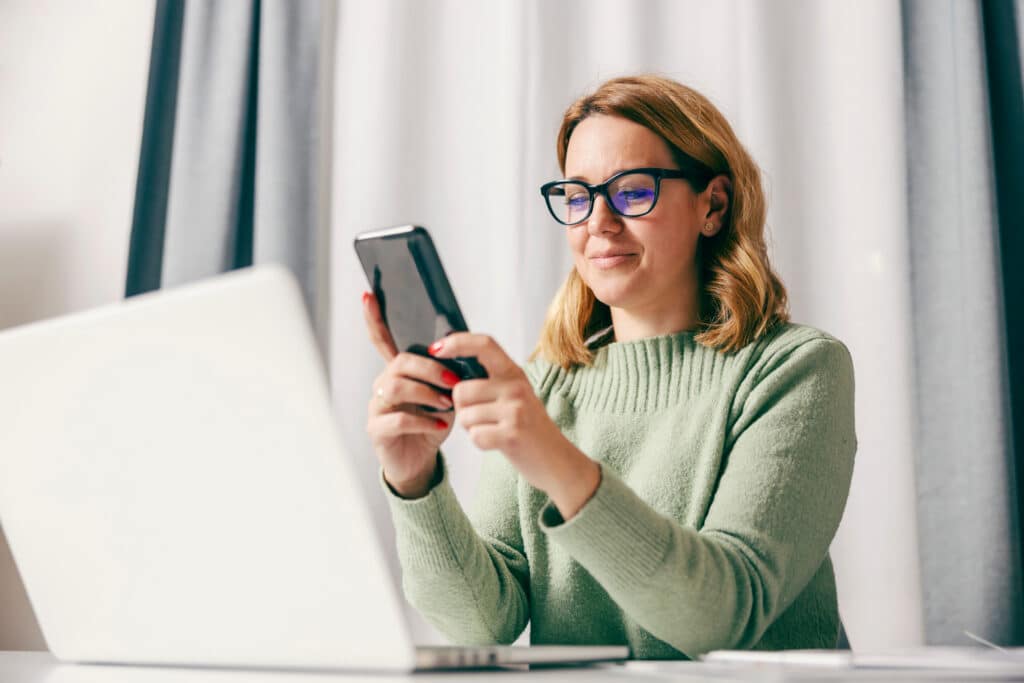 How Secure Patient Messaging Improves Care Coordination A happy entrepreneur using smart phone while working online at her home office.