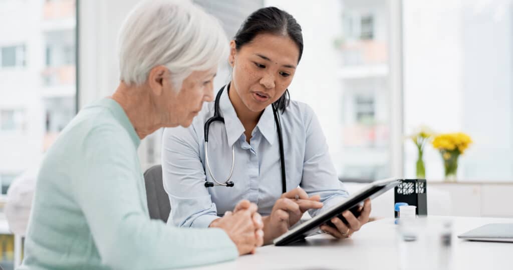 Results, tablet and senior woman with doctor talking about healthcare data, report or communication in elderly care or consultation. Patient, nurse and advice in meeting with medical worker or expert.